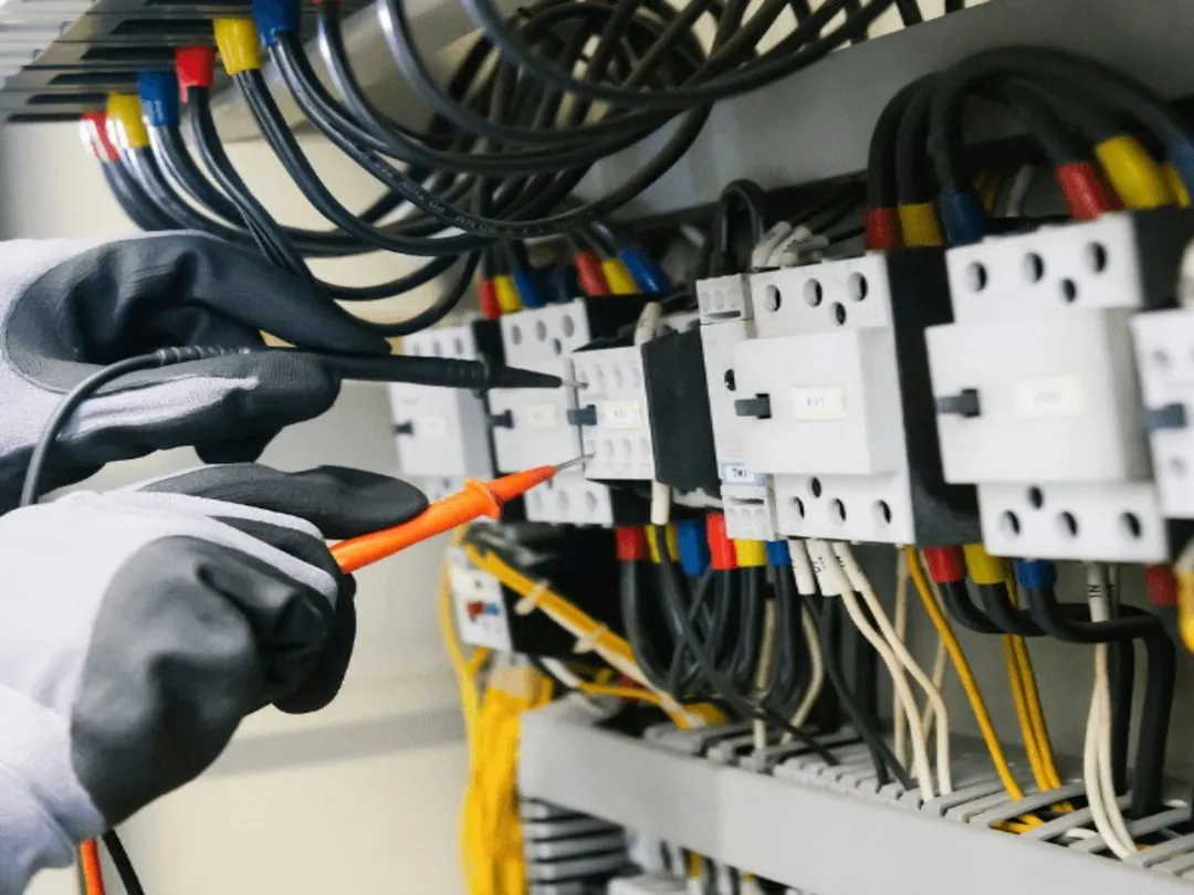 Technician testing electrical connections and checking voltage on an AC unit - best time of year to schedule your ac tune up